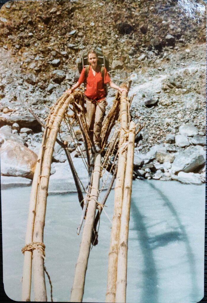 Young woman with backpack walks across bamboo bridge in Nepaloss